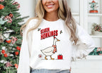 Woman wearing a White Season Honkings Christmas sweatshirt with a festive goose graphic while enjoying a coffee outdoors.
