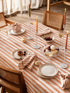 Soft terracotta and cream striped cotton twill tablecloth styled on a dining table with candles, ceramic plates, and neutral tableware.