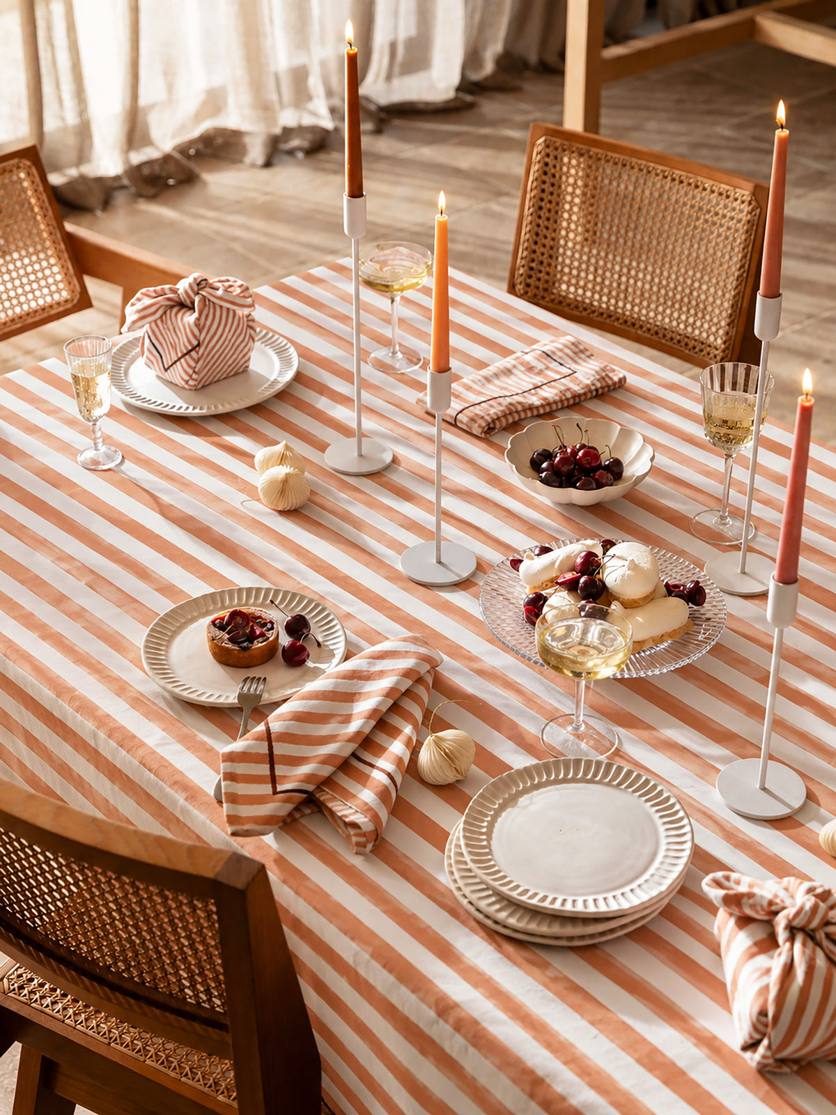 Soft terracotta and cream striped cotton twill tablecloth styled on a dining table with candles, ceramic plates, and neutral tableware.
