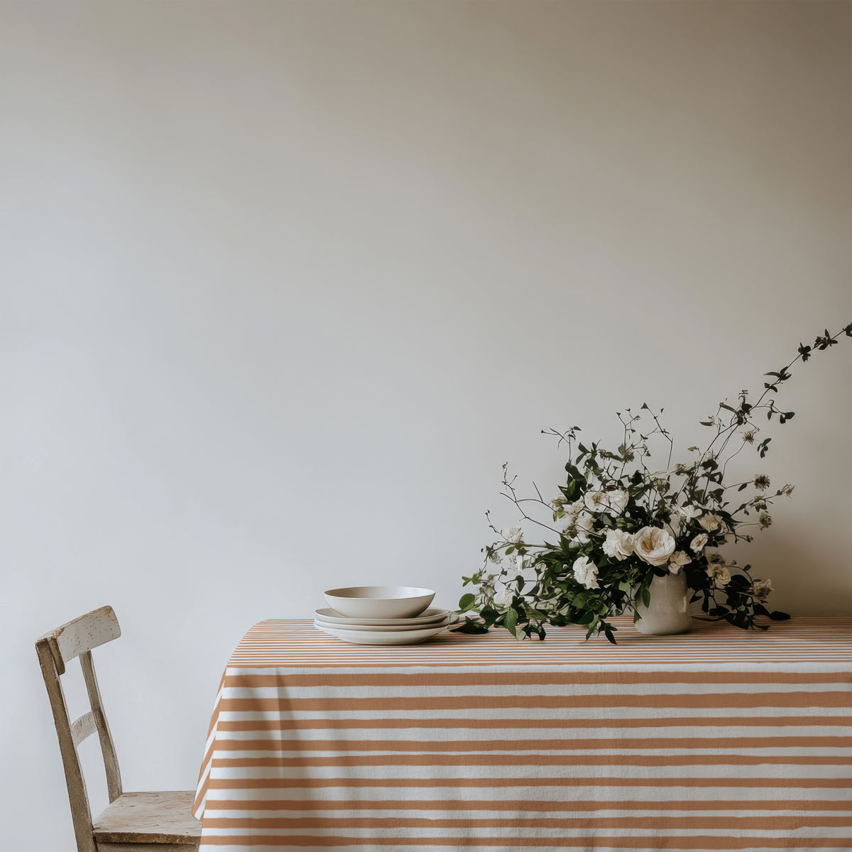 Soft terracotta striped cotton tablecloth draped over a dining table, showcasing its delicate linear pattern and natural fabric texture.