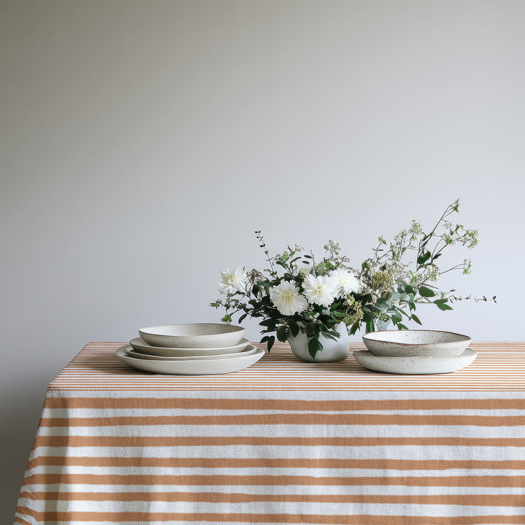 Square terracotta and cream striped cotton tablecloth styled on a dining table for an intimate Mediterranean-inspired setting.