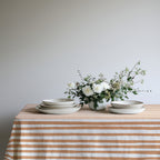 Square terracotta and cream striped cotton tablecloth styled on a dining table for an intimate Mediterranean-inspired setting.
