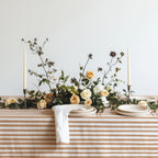Modern Mediterranean dining table dressed with a terracotta and cream striped tablecloth, neutral ceramics, and warm candlelight.