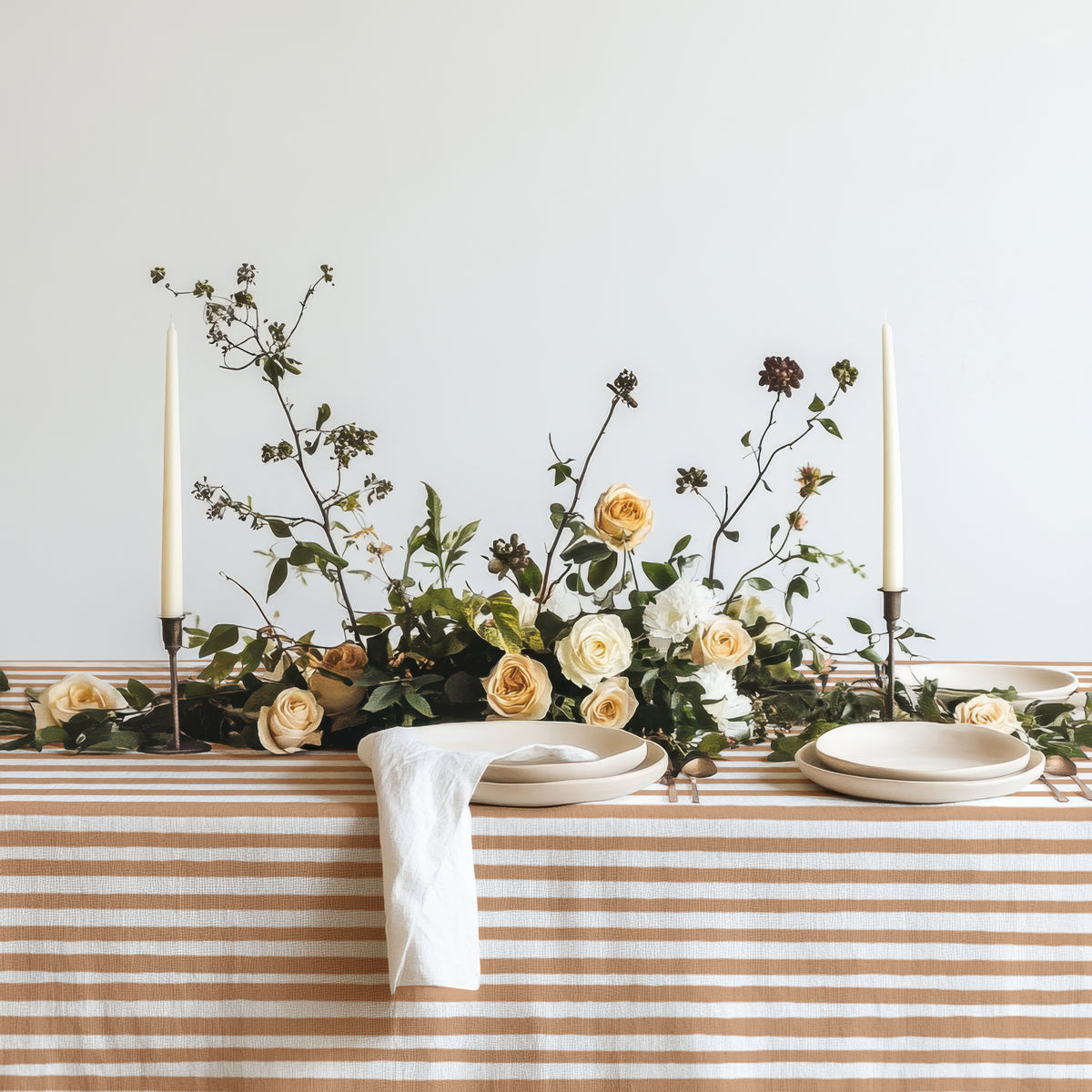 Modern Mediterranean dining table dressed with a terracotta and cream striped tablecloth, neutral ceramics, and warm candlelight.