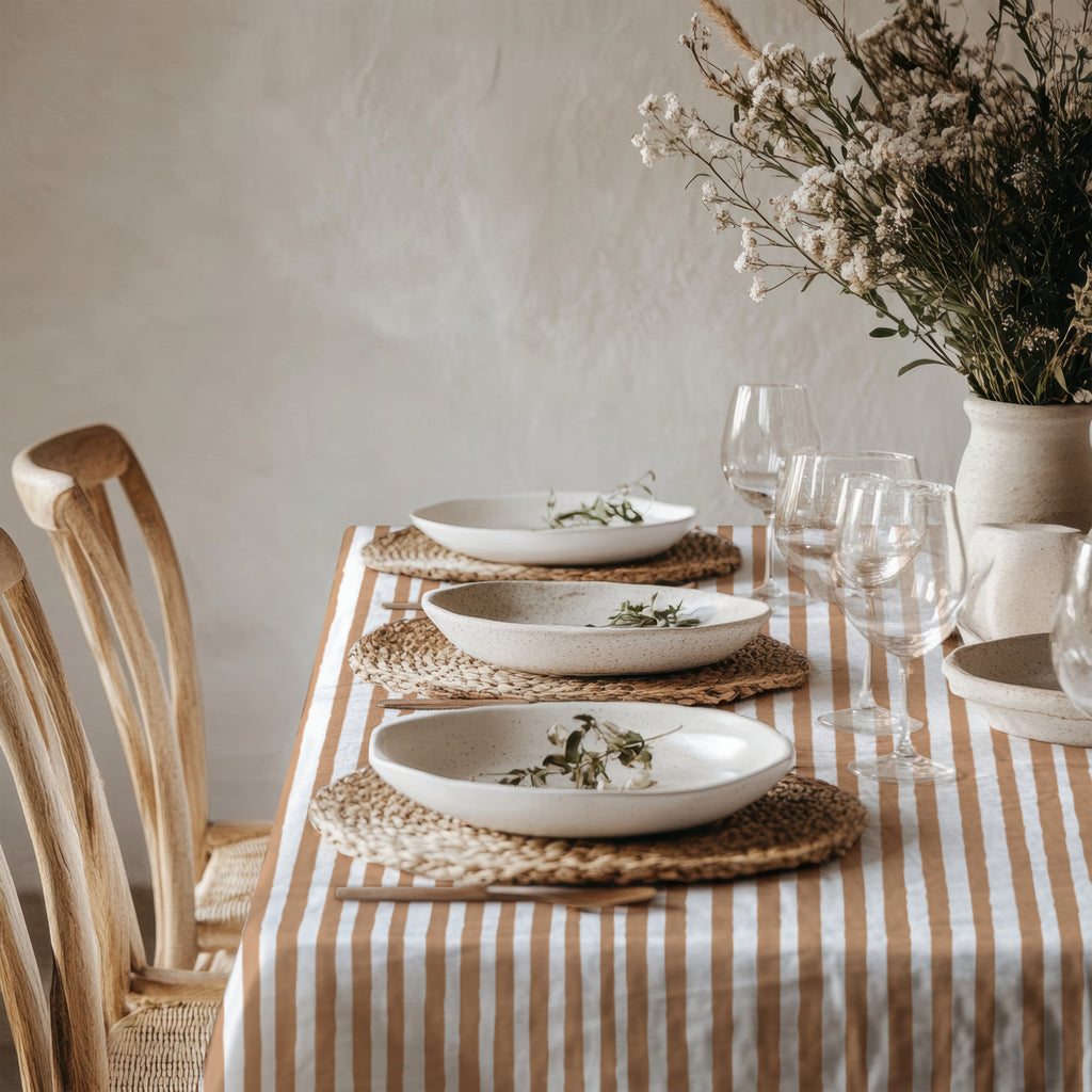 Rectangular terracotta striped cotton tablecloth styled for a long dining table with coordinated plates, glasses, and candles.