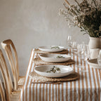 Rectangular terracotta striped cotton tablecloth styled for a long dining table with coordinated plates, glasses, and candles.