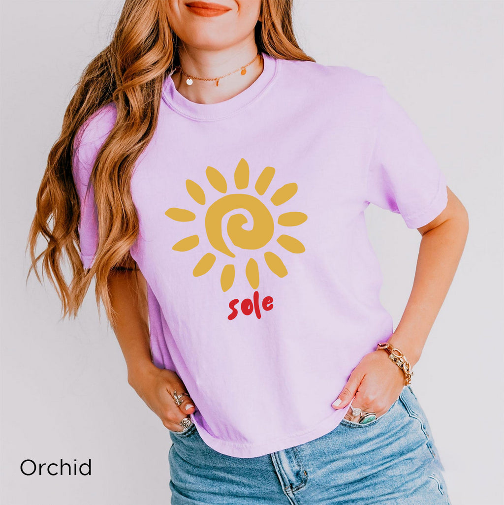 Lifestyle image: Woman wearing the SOLE T-shirt during a relaxed outdoor moment, highlighting the minimalist golden sun graphic and casual boxy fit.