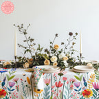 Colourful Mediterranean wildflower meadow tablecloth featuring hand-drawn floral illustrations styled on a modern dining table with neutral ceramics