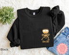 Folded black “A Tini Bit Older” embroidered martini sweatshirt on white textured surface with jeans and greenery, cozy bachelorette party sweatshirt for women.