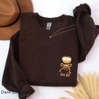 Folded dark chocolate “A Tini Bit Older” embroidered martini sweatshirt with rolled sleeves, styled with brown hat, casual birthday or cocktail party outfit for women.