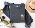Folded dark heather grey “A Tini Bit Older” embroidered martini sweatshirt, rolled sleeves, displayed with neutral autumn-themed decor, cozy and fun birthday sweatshirt.