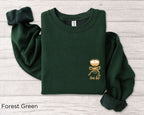 Folded forest green “A Tini Bit Older” embroidered martini sweatshirt, rolled sleeves, styled with cotton stems and wooden props, perfect women’s bachelorette or birthday gift.
