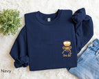 Folded navy “A Tini Bit Older” embroidered martini sweatshirt, rolled sleeves, paired with denim jeans, fun and cozy women’s birthday or party outfit.