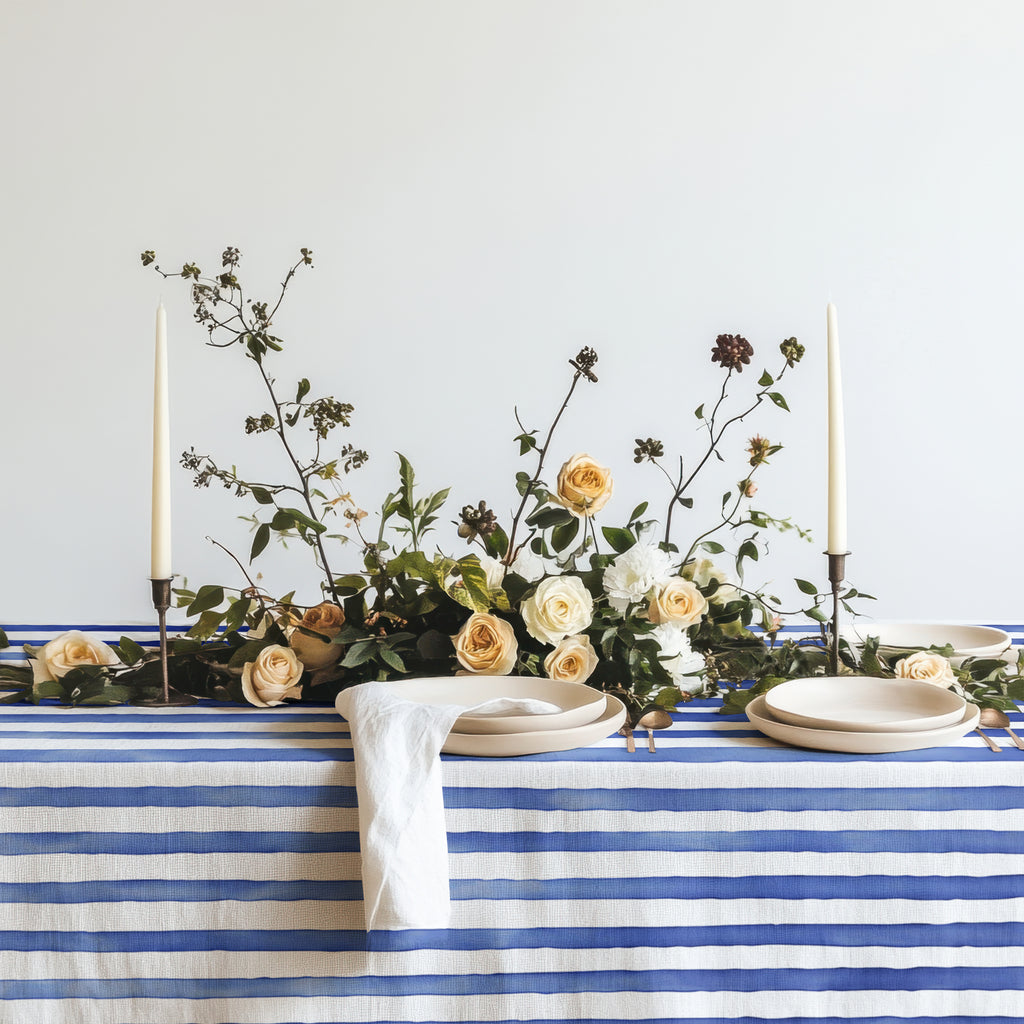 Close-up of the watercolor blue and white striped cotton twill tablecloth on a dining table with neutral-toned tableware, showcasing the fine quality fabric.