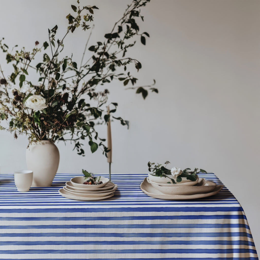 Cotton twill tablecloth with watercolor blue stripes, evoking the relaxed Mediterranean vibe, beautifully styled with fresh flowers and neutral plates for a breezy, coastal dining look.