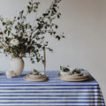 Cotton twill tablecloth with watercolor blue stripes, evoking the relaxed Mediterranean vibe, beautifully styled with fresh flowers and neutral plates for a breezy, coastal dining look.