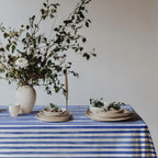 Cotton twill tablecloth with watercolor blue stripes, evoking the relaxed Mediterranean vibe, beautifully styled with fresh flowers and neutral plates for a breezy, coastal dining look.