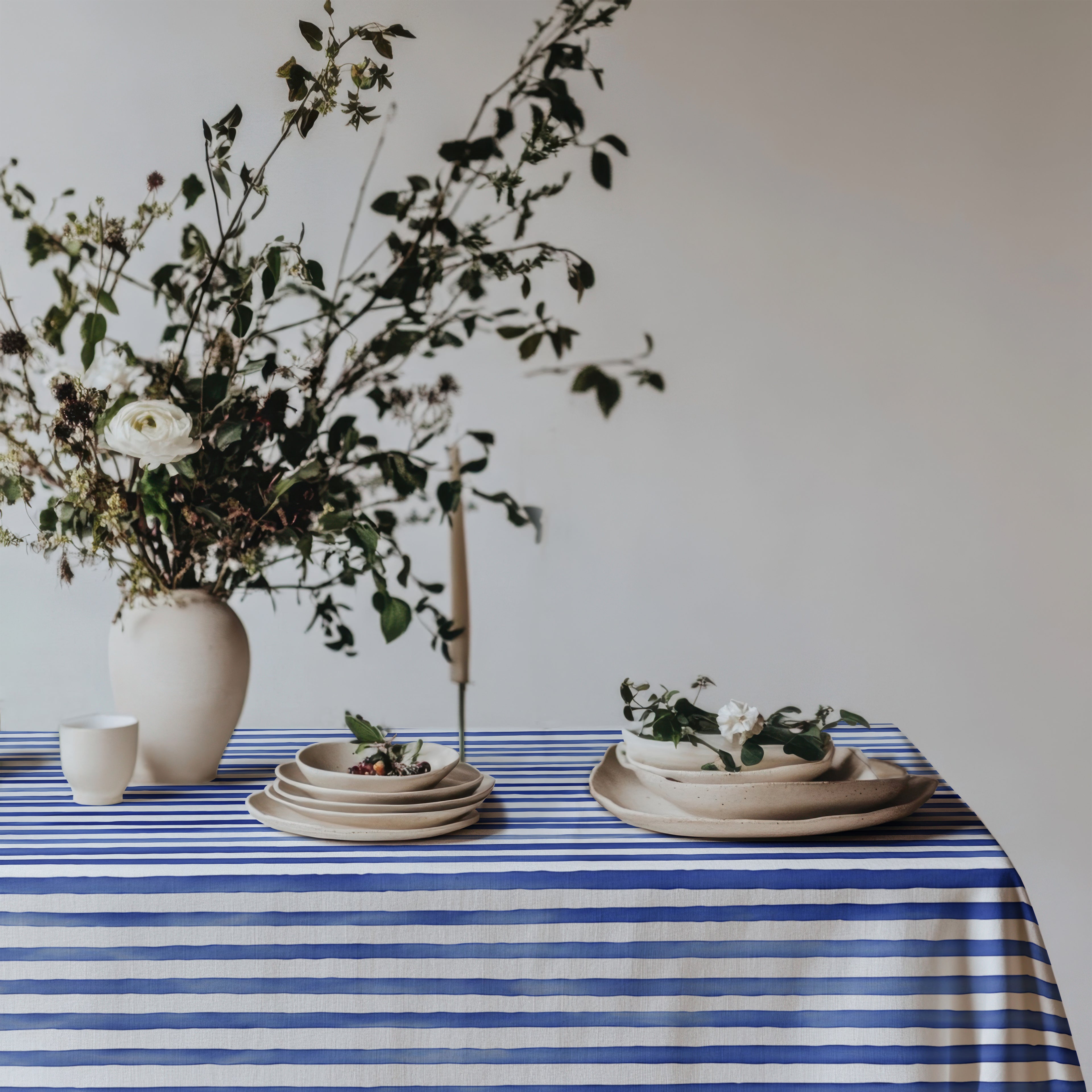 Cotton twill tablecloth with watercolor blue stripes, evoking the relaxed Mediterranean vibe, beautifully styled with fresh flowers and neutral plates for a breezy, coastal dining look.